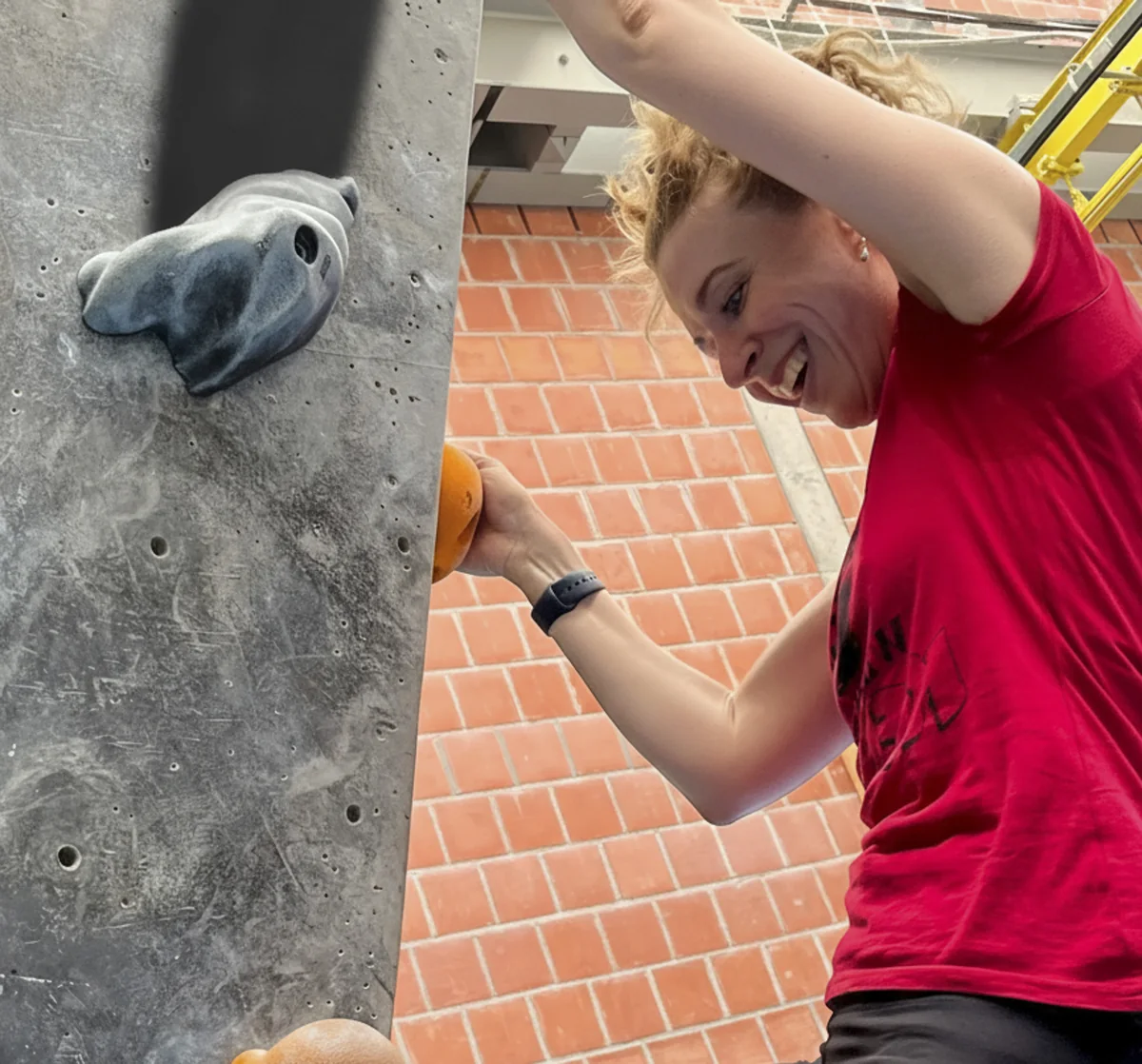 Kollegin an der Kletterwand, lachend im Zug zum nächsten Griff